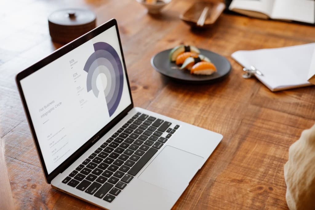 Ordinateur portable sur table en bois, écran affichant un tableau de bord infographie — espace de travail moderne pour illustrer Kames-CRM.